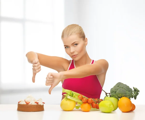 Woman with fruits showing thumbs down to cake