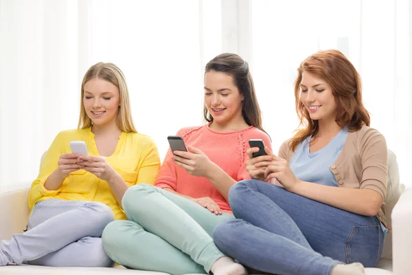 Smiling teenage girls with smartphones at home