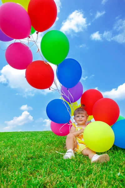 Toddler girl sitting a bunch of balloons