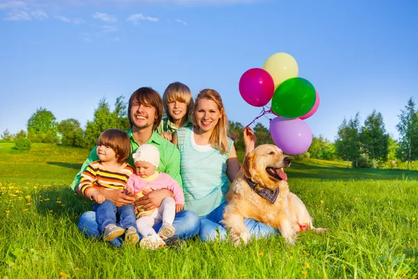 Smiling family sit on grass with balloons and dog