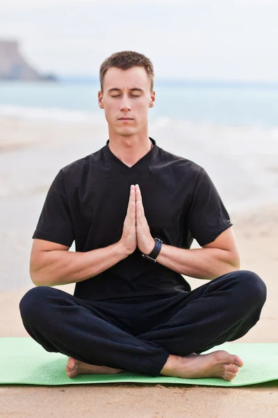 Young man doing yoga on the beach
