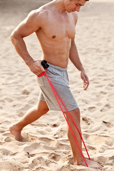 Young athletic man exercising and doing fitness with a chest expander(resistance band ) on the beach