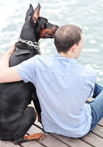 A man and a sitting dog looking out at the ocean.