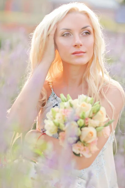 Pretty blond woman sitting on lavender field. Wedding. Bride with bouquet.