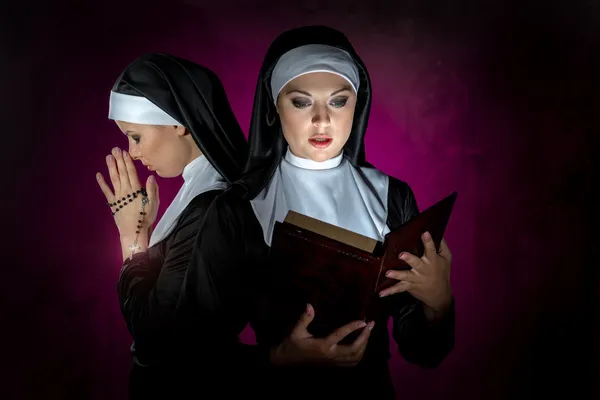 Two attractive young nuns with beads and bible praying