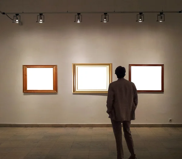 Man in gallery room looking at empty picture frames