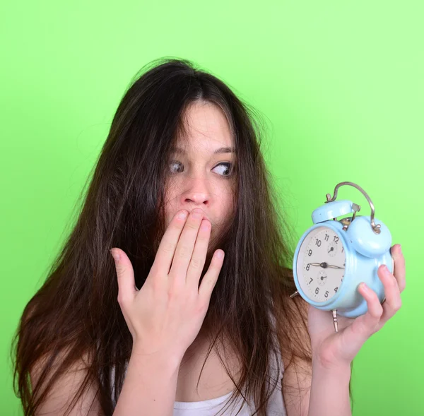 Portrait of sleepy young female in chaos holding clock against g