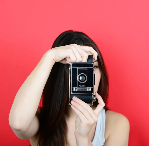 Portrait of young female holding vintage camera against red back