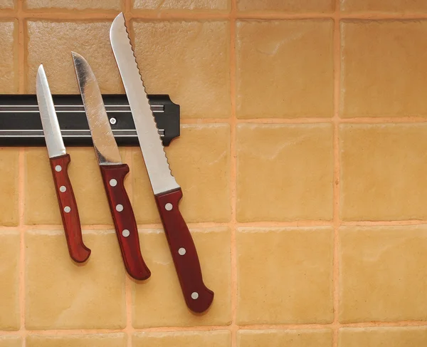A set of knifes are hanging on a kitchen wall.
