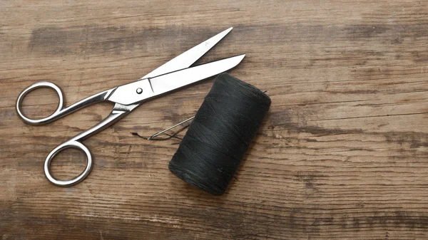 Sewing kit. Scissors with thread and needles on wooden table