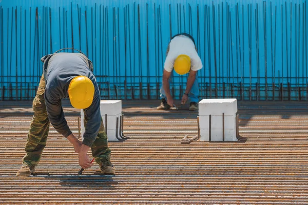 Construction workers installing binding wires to steel bars