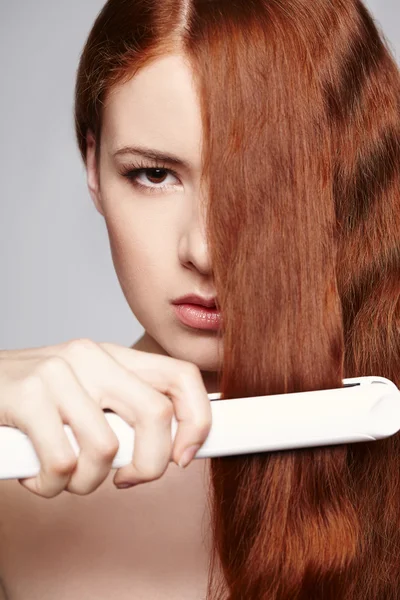 Redheaded woman with hair straightening irons