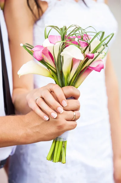 Closeup view of a bride and groom's hands with bouquet of callas