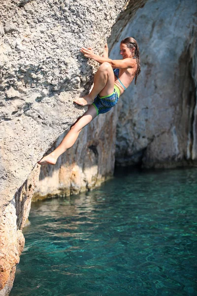 Deep water soloing, young female rock climber on face of cliff