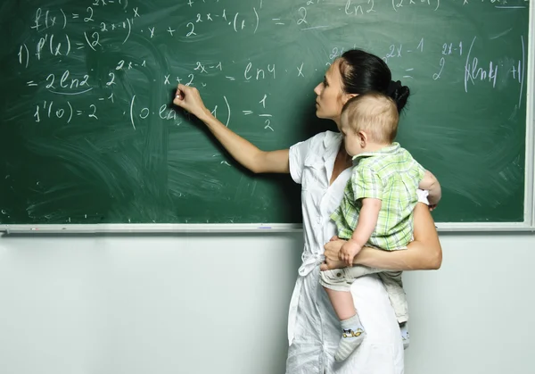 Yang mom with baby boy is writing down formulas in the class board