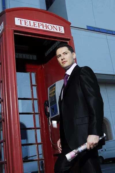 Successful yang man in business suit posing in front of vintage phone booth