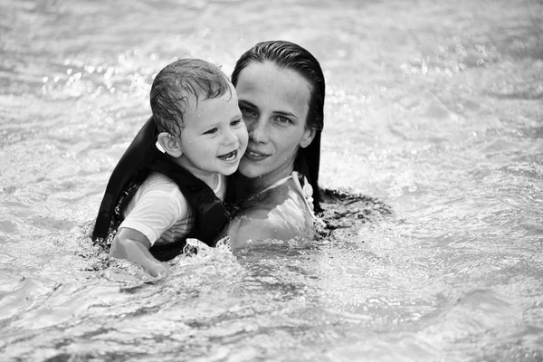 Beautiful young mom plays in the pool with her baby son