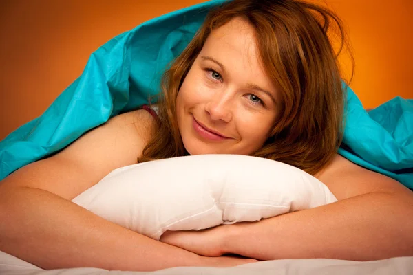 Woman iling on pillow in bed, covered with blanket