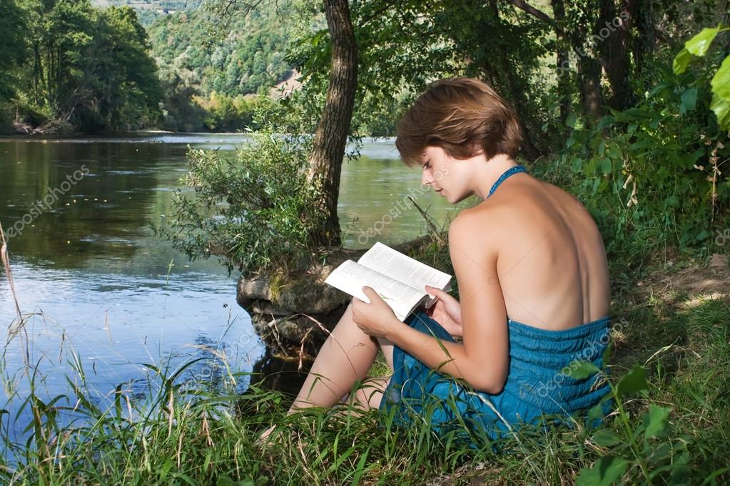 Belle jeune femme, assis près de la rivière et lire un livre — Photo