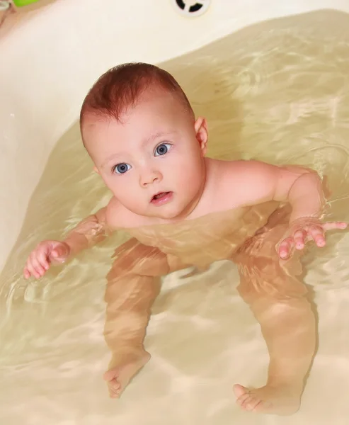 Baby washing and swimming in bath water with fun look