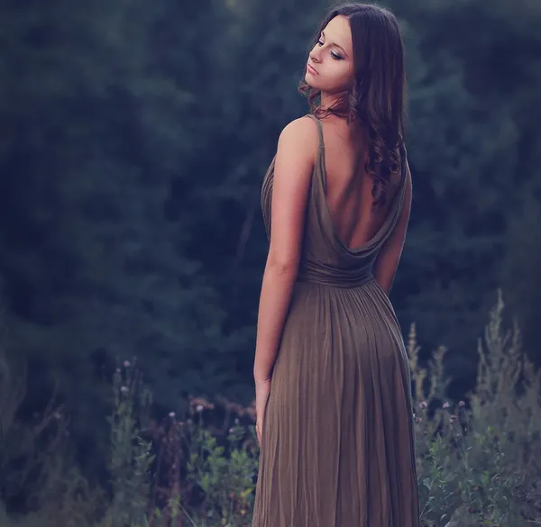 Sexy woman standing in dress with nude back on nature background