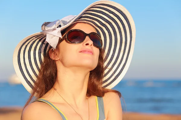 Beautiful woman in hat and sun glasses looking up and joy on blue sea background