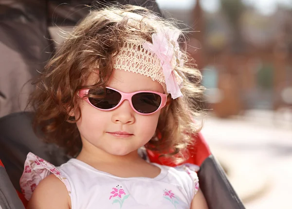 Beautiful small girl with curly hair and pink sunglasses