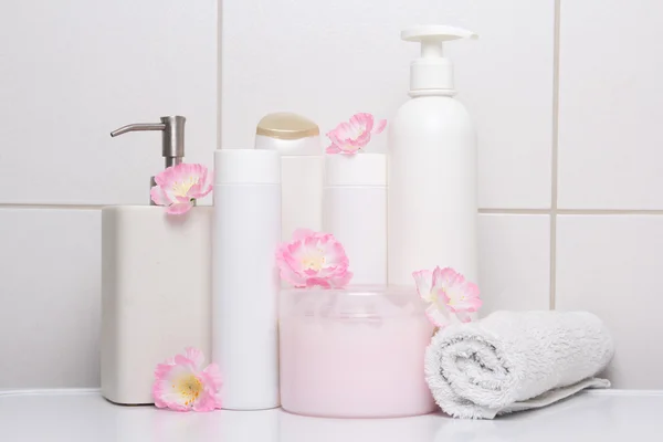 Set of white cosmetic bottles with pink flowers over tiled wall