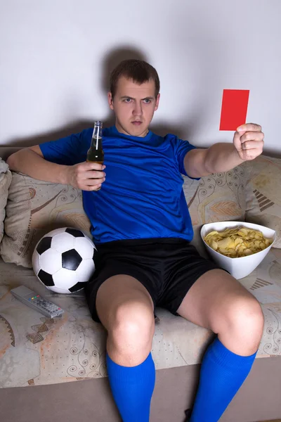 Young man watching football on tv at home and showing penalty ca