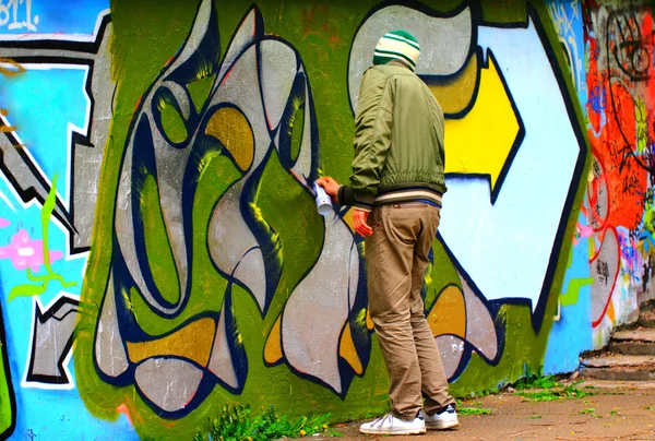 A young man makes graffiti on the concrete fence