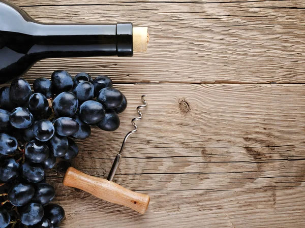 Bottle of wine, corkscrew and grape on wooden background