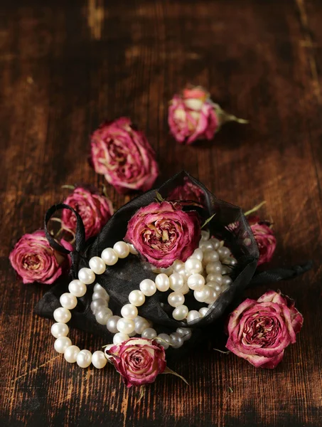 Vintage pearl with dry roses on a wooden background