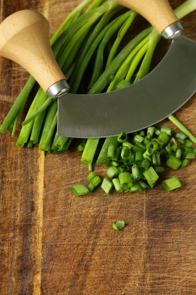 Fresh green chives on wooden board with a special knife