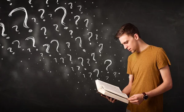 Young man reading a book with question marks coming out from it