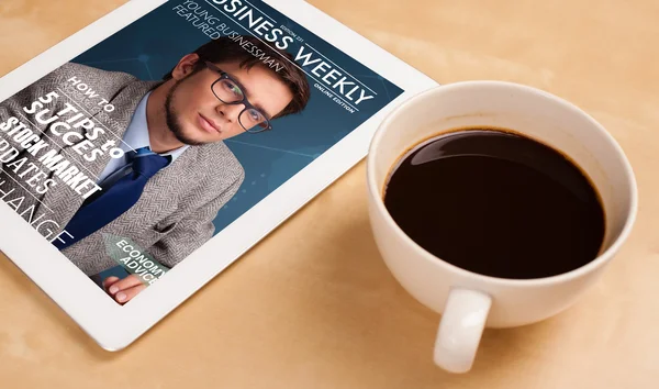 Tablet pc showing magazine on screen with a cup of coffee on a d