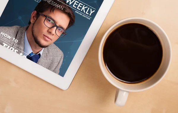 Tablet pc showing magazine on screen with a cup of coffee on a d