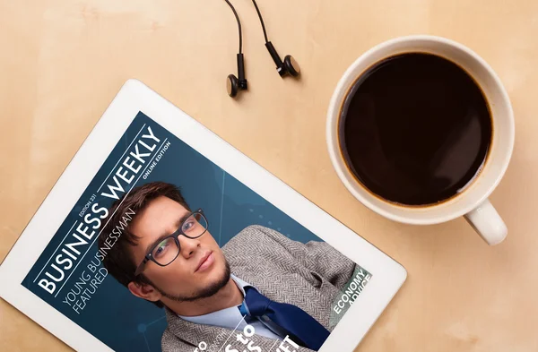 Tablet pc showing magazine on screen with a cup of coffee on a d