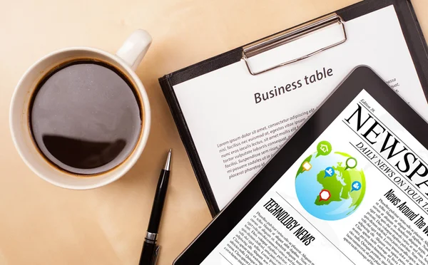 Tablet pc shows news on screen with a cup of coffee on a desk