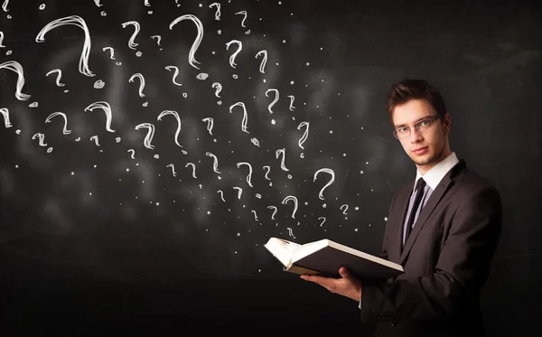 Young man reading a book with question marks coming out from it