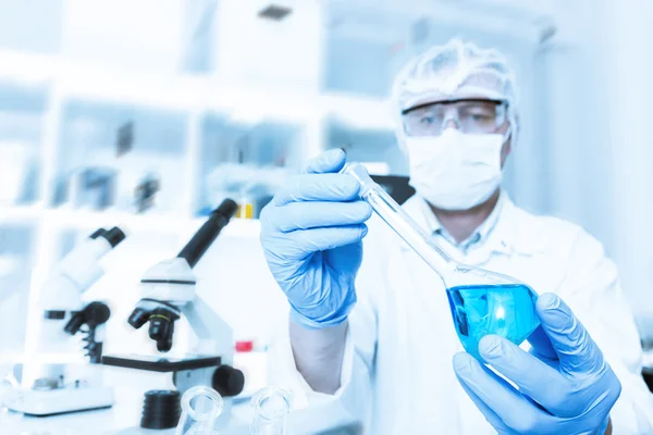 Scientist working in the lab, in protective mask , examines a with liquid