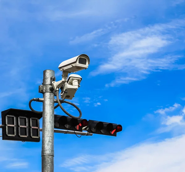 Surveillance camera and traffic light against blue sky