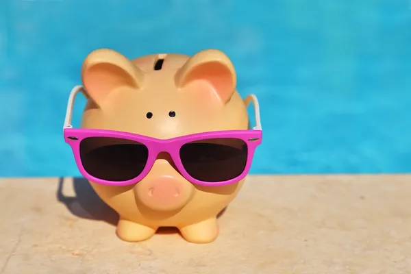 Summer piggy bank with sunglasses in front of a swimming pool