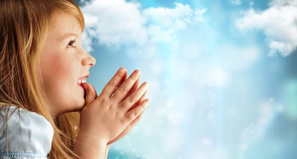 Portrait of young smiling praying girl in blue dress against sky