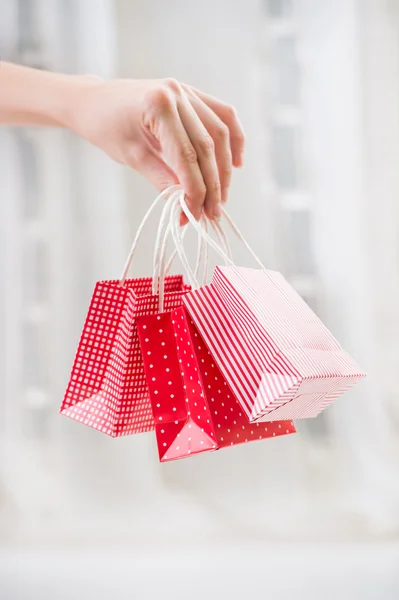 Female hand holding red gift bag with presents with her fingers