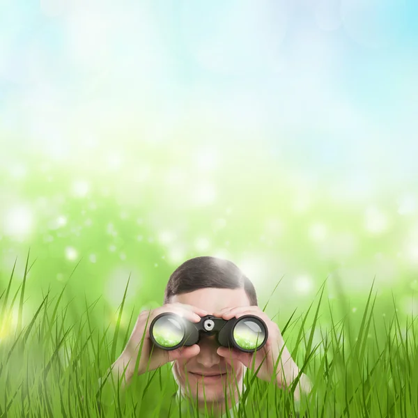 Man looking through binoculars from grass