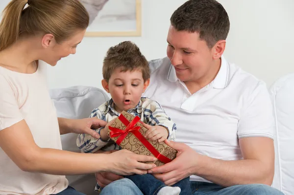 Couple giving gift to their little son in the living room.