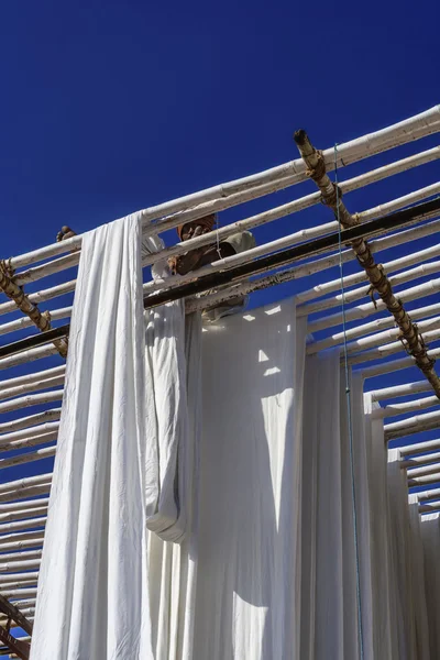 Indian man hanging cotton clothes to dry under the sun