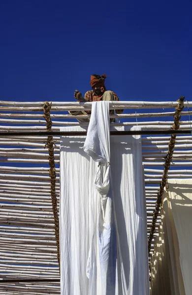 Indian man hanging cotton clothes to dry under the sun