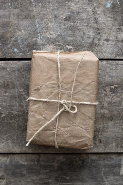 Package wrapped in wrinkled brown paper lying on weathered wood