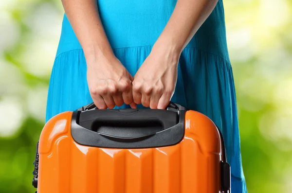 Woman in blue dress holds orange suitcase in hands on natural ba